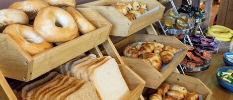 A breakfast buffet with various breads, pastries, and fruits.