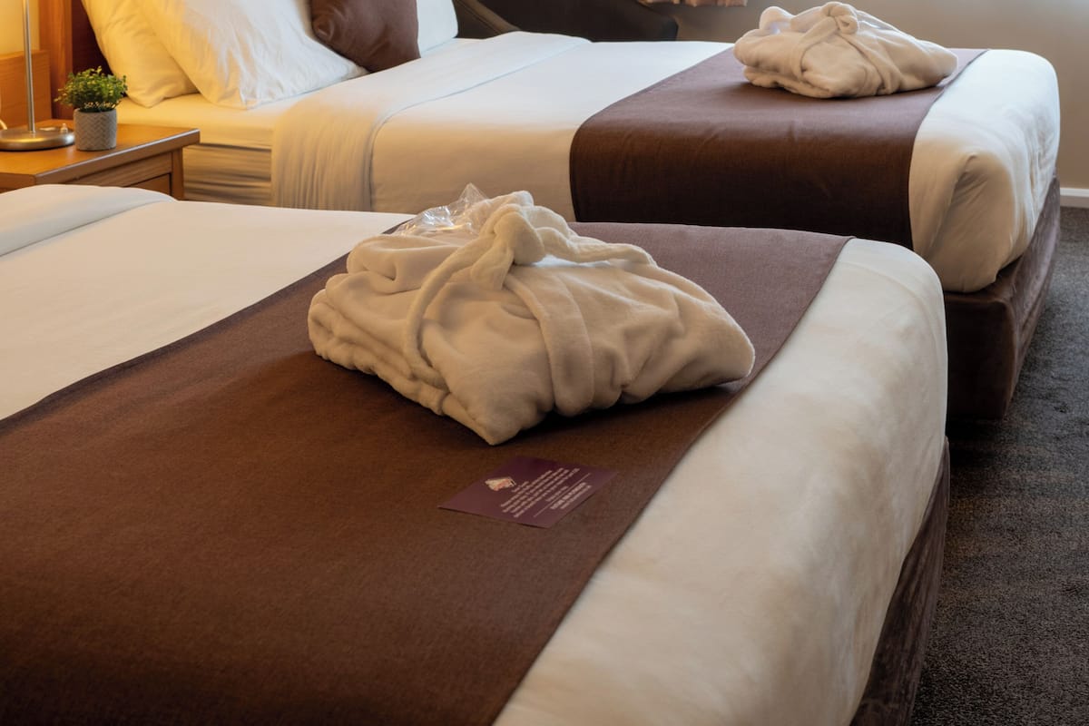 Habitació d'hotel amb dos llits, una taula de nit, una cadira, una làmpada i una finestra amb cortines.