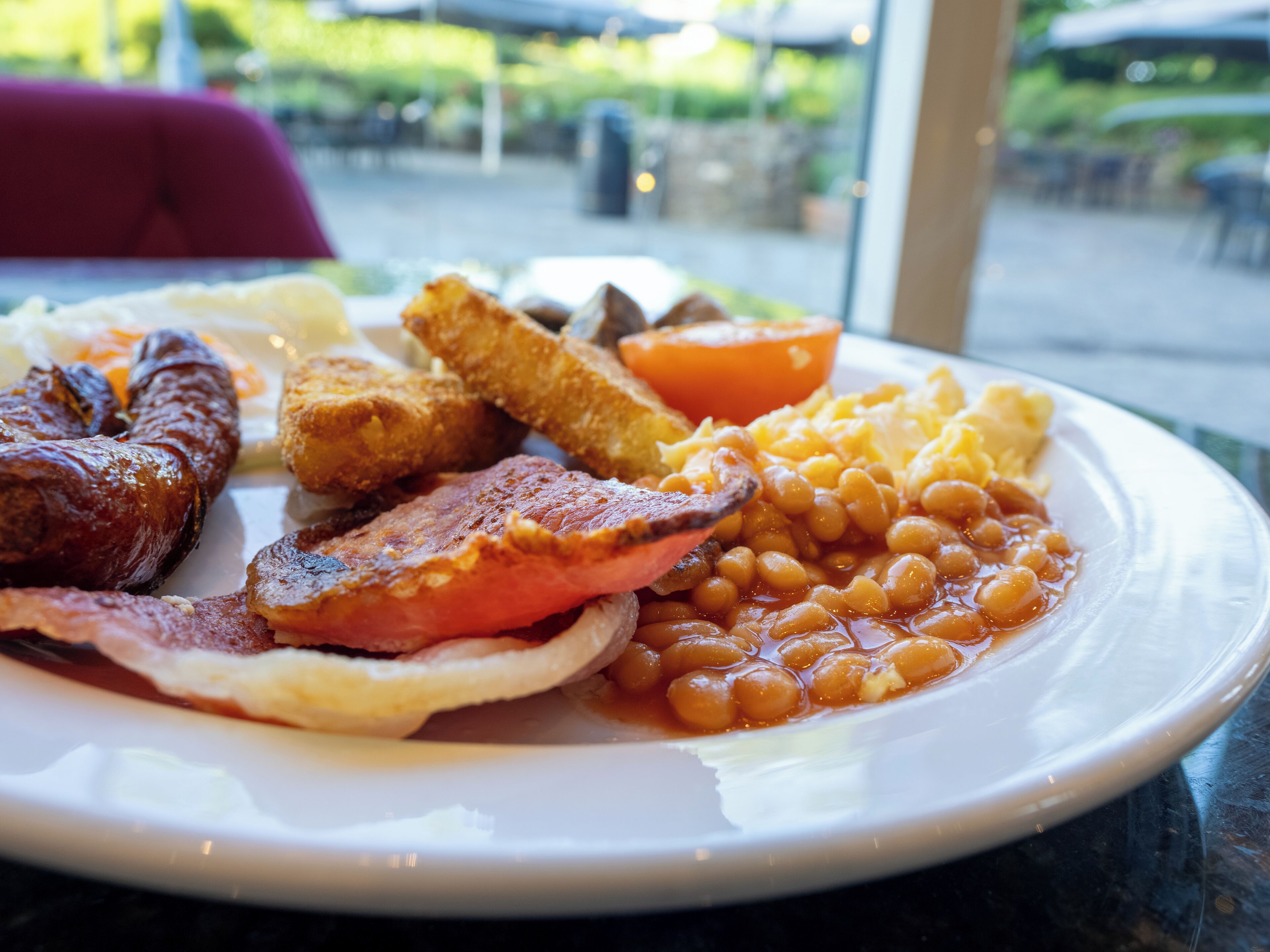 A plate of breakfast food including sausages, bacon, beans, and toast.