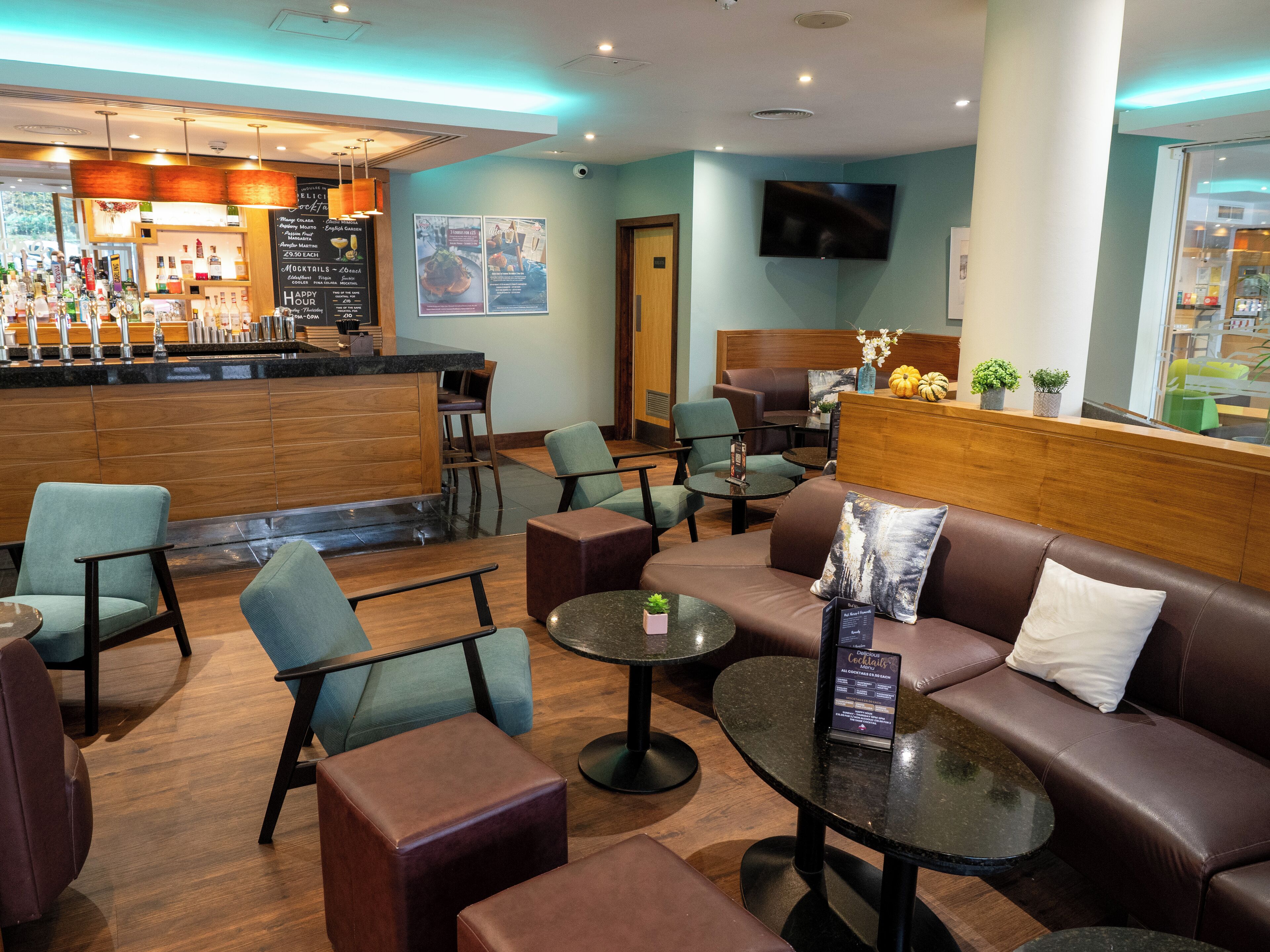 A modern bar area with seating arrangements including sofas and tables, a counter with various bottles, and a television mounted on the wall.