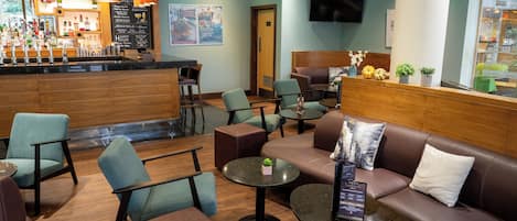 A modern bar area with seating arrangements including sofas and tables, a counter with various bottles, and a television mounted on the wall.