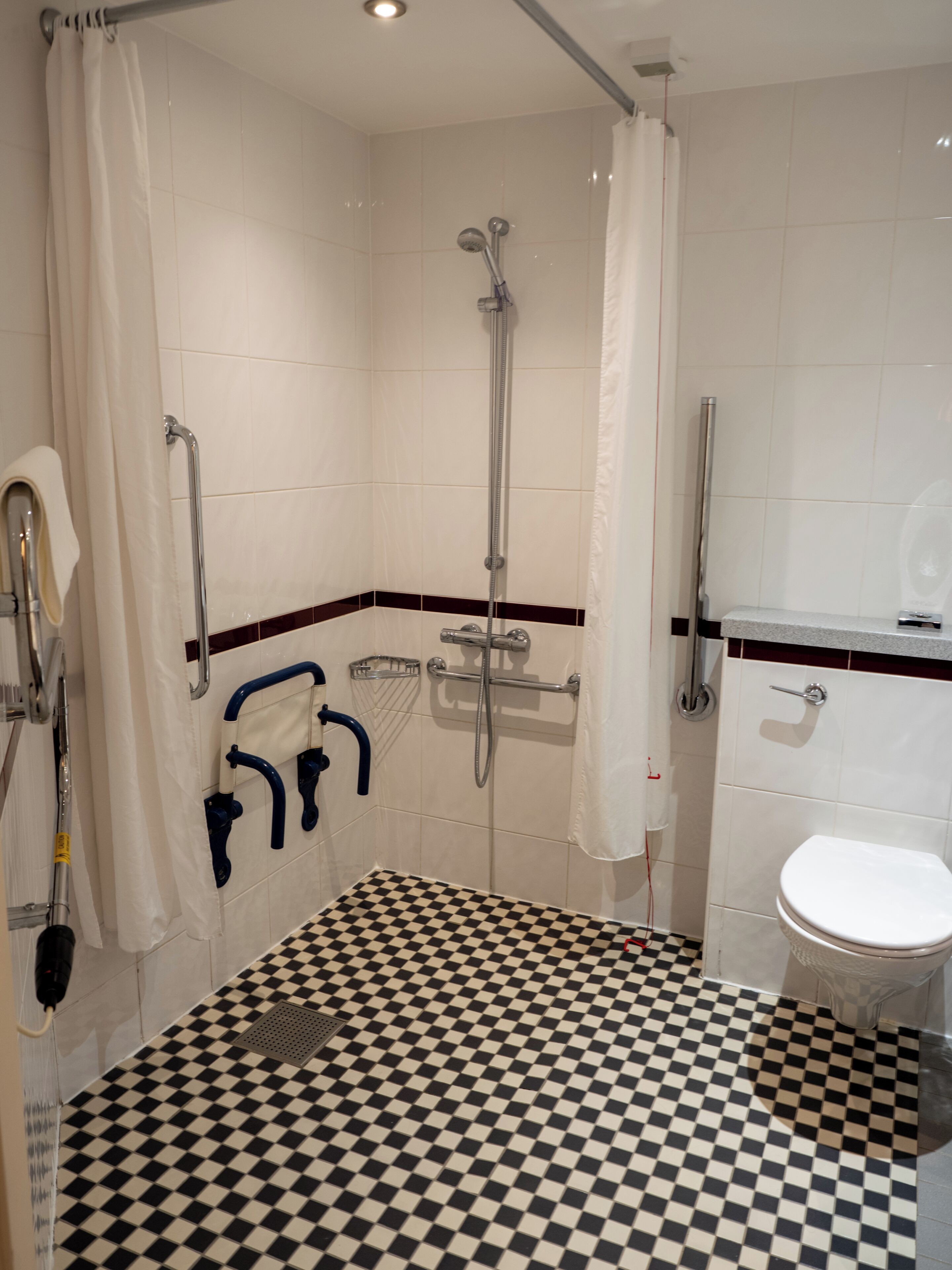 A bathroom with a checkered floor, a shower with a grab bar, a toilet, and a sink.