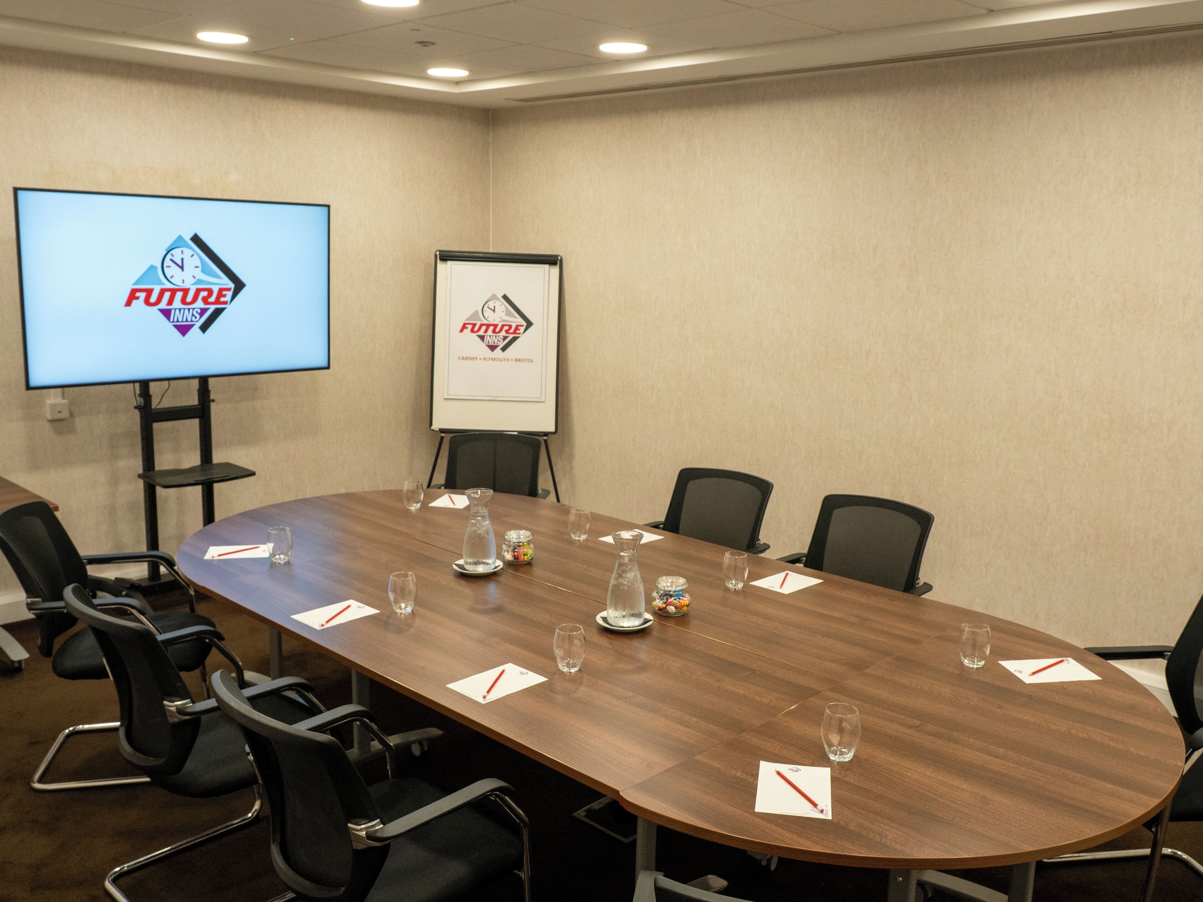 A conference room with a long table, chairs, a projector screen, and a whiteboard.