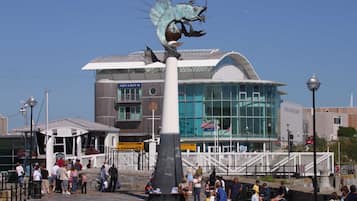 A public square with a large sculpture of a fish, a modern building labeled "Aquarium," and a crowd of people.