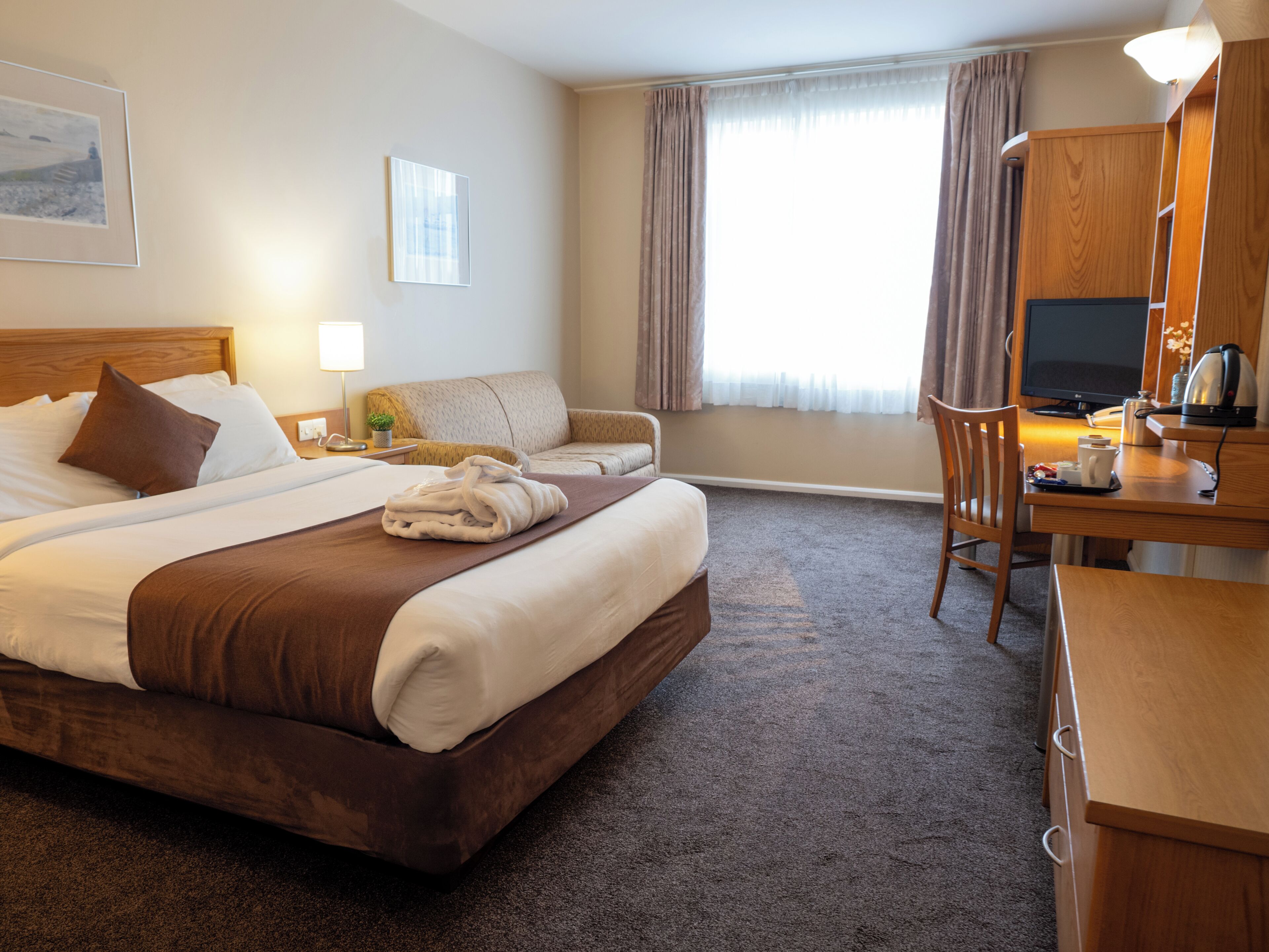 A hotel room with a large bed, a desk, a chair, a television, and a window with curtains.