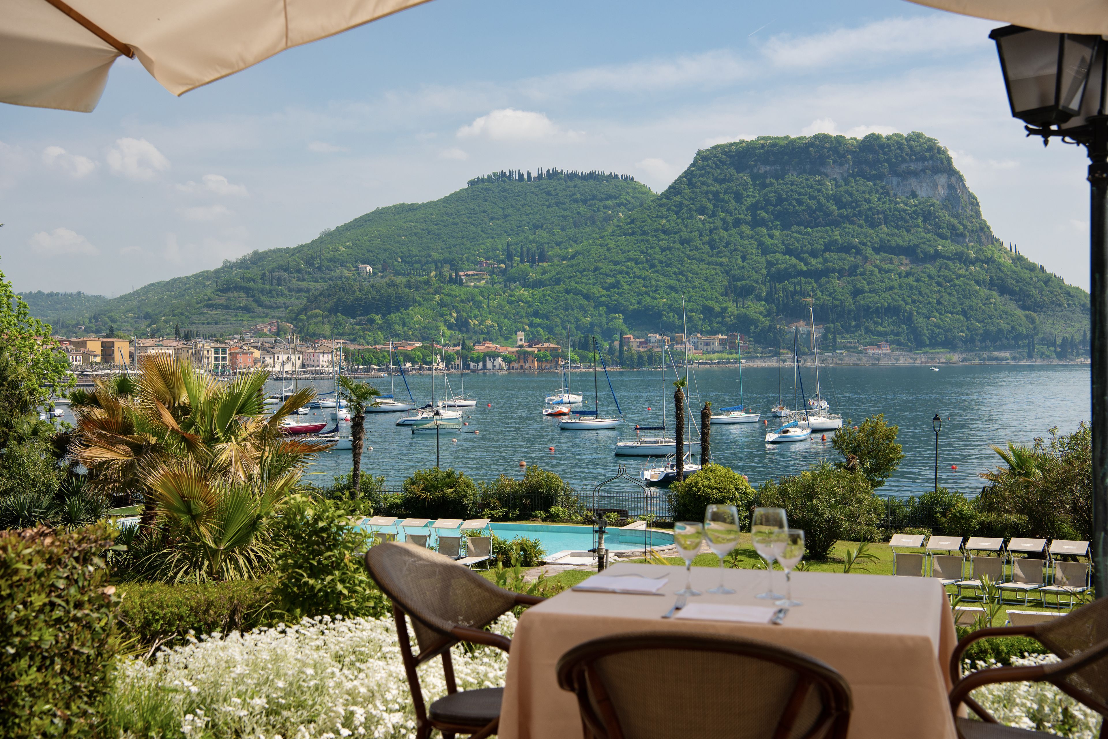 Una terraza con mesa lista para comer, con vistas a un puerto deportivo con barcos y montañas al fondo.