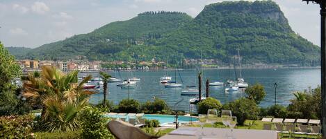 A terrace with a table set for dining, overlooking a marina with boats and a mountain backdrop.