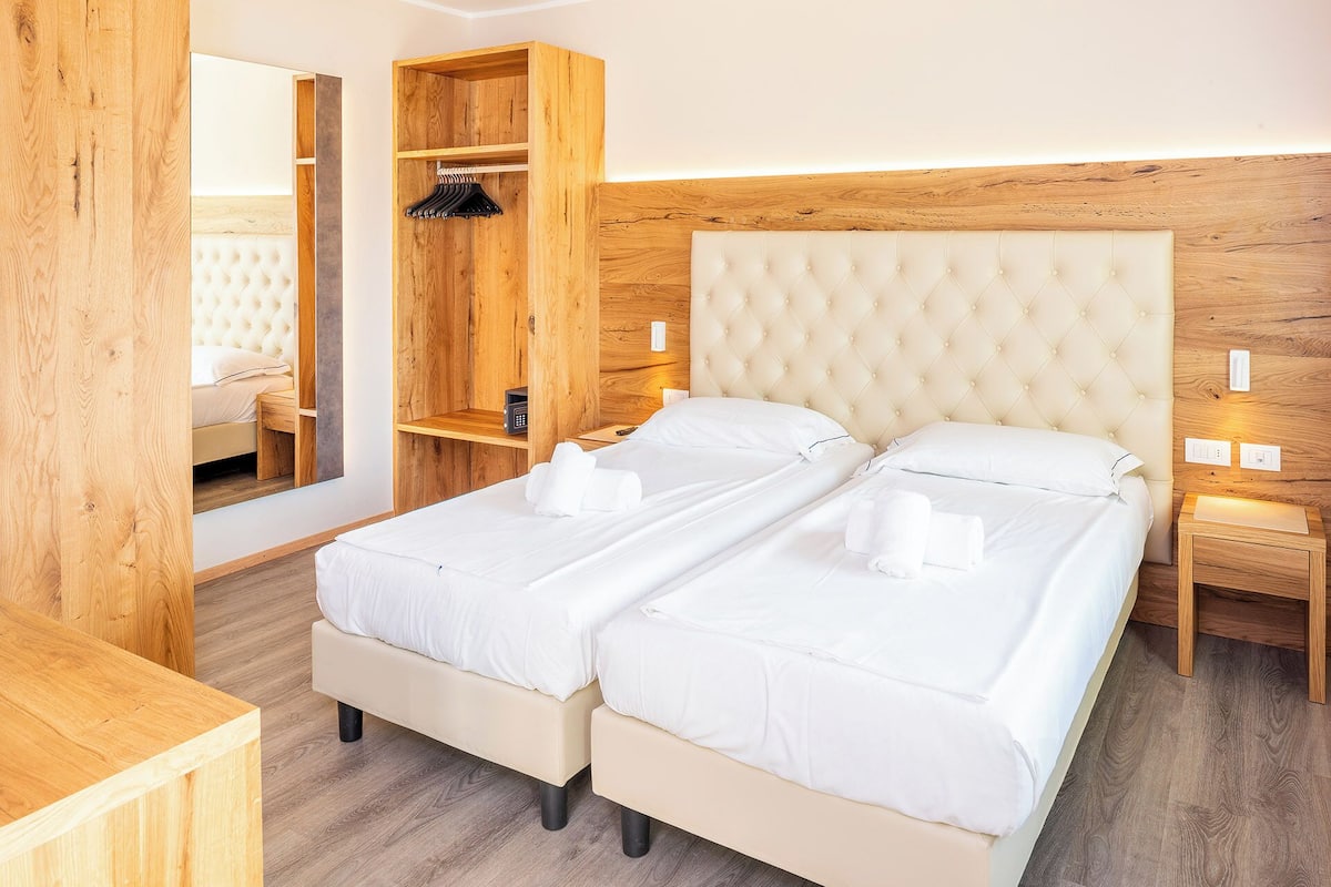 A double bed with a tufted headboard, a wooden wardrobe, and a bedside table with a lamp.