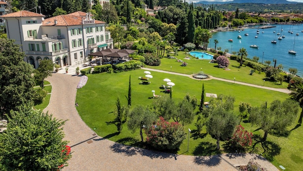 A hotel with a swimming pool, a garden, and a view of the lake with boats. - Hotel Du Parc (Garda)