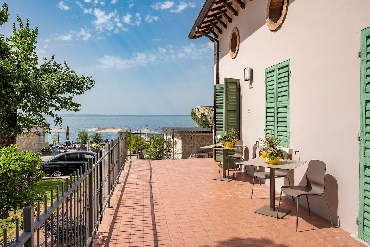 A terrace with a view of the sea, a table with chairs, and a car parked nearby.