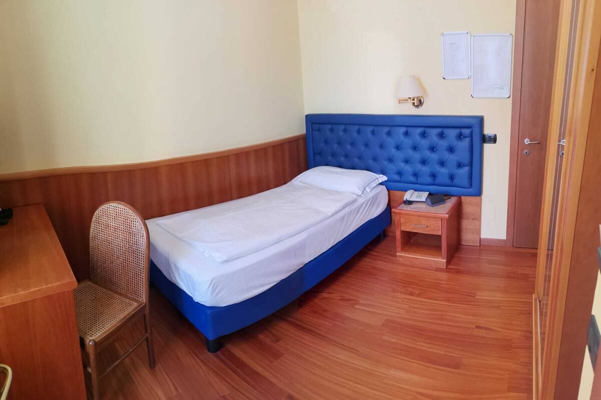 A single bed with a blue headboard in a room with wooden flooring and a wooden desk.