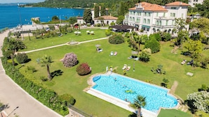 A large hotel with a swimming pool, surrounded by lush greenery and a view of the sea. - Hotel Du Parc (Garda)