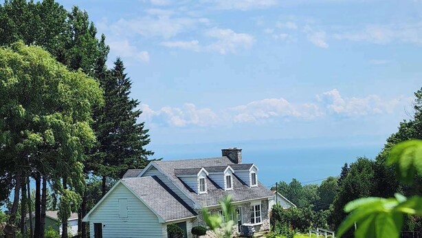 A house with a stone chimney, a garage, and a well-maintained lawn. - Auberge des Nuages (La Malbaie)