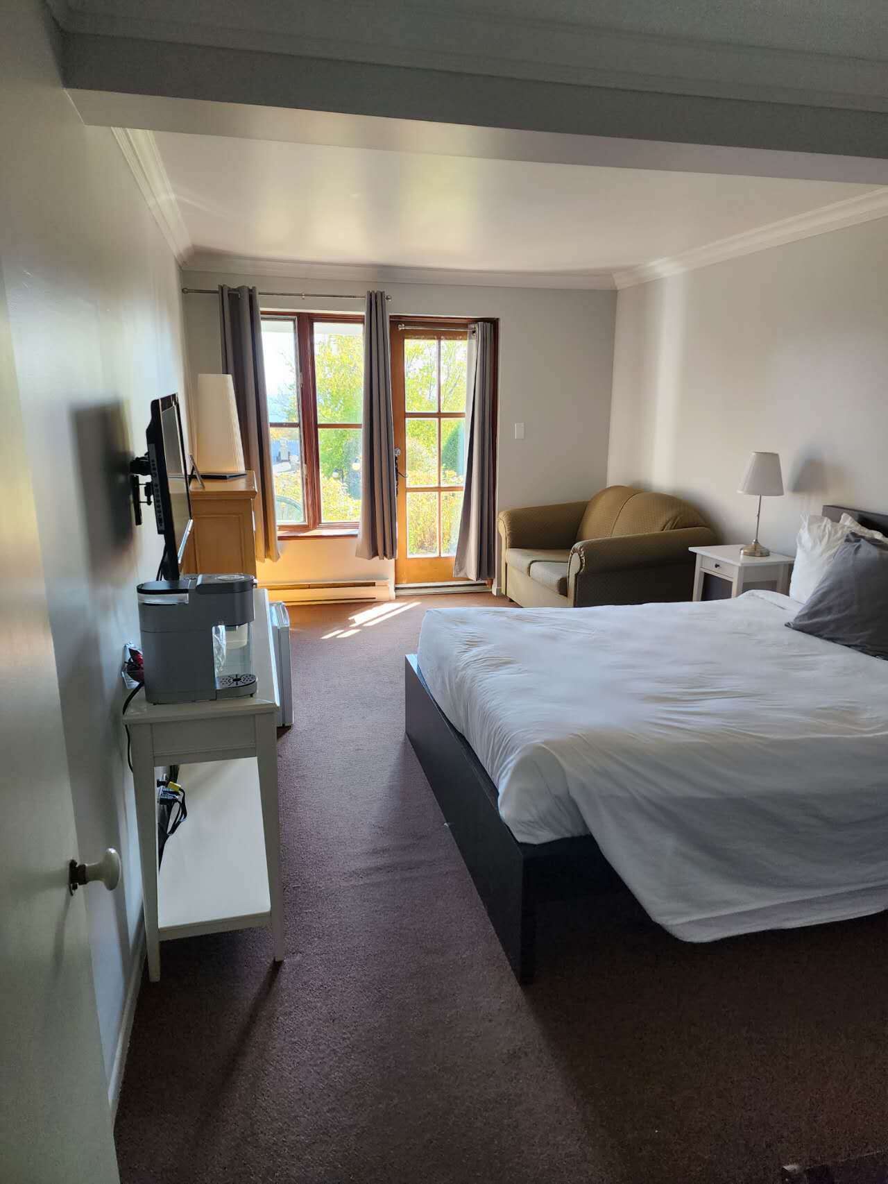 Una habitación de hotel con cama, escritorio con computadora, silla y ventana con cortinas.