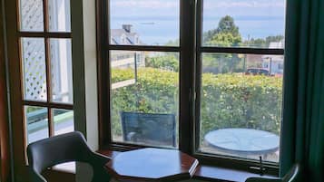 A room with a table and two chairs, a window with a view of the sea and buildings, and a door with a patterned glass panel.