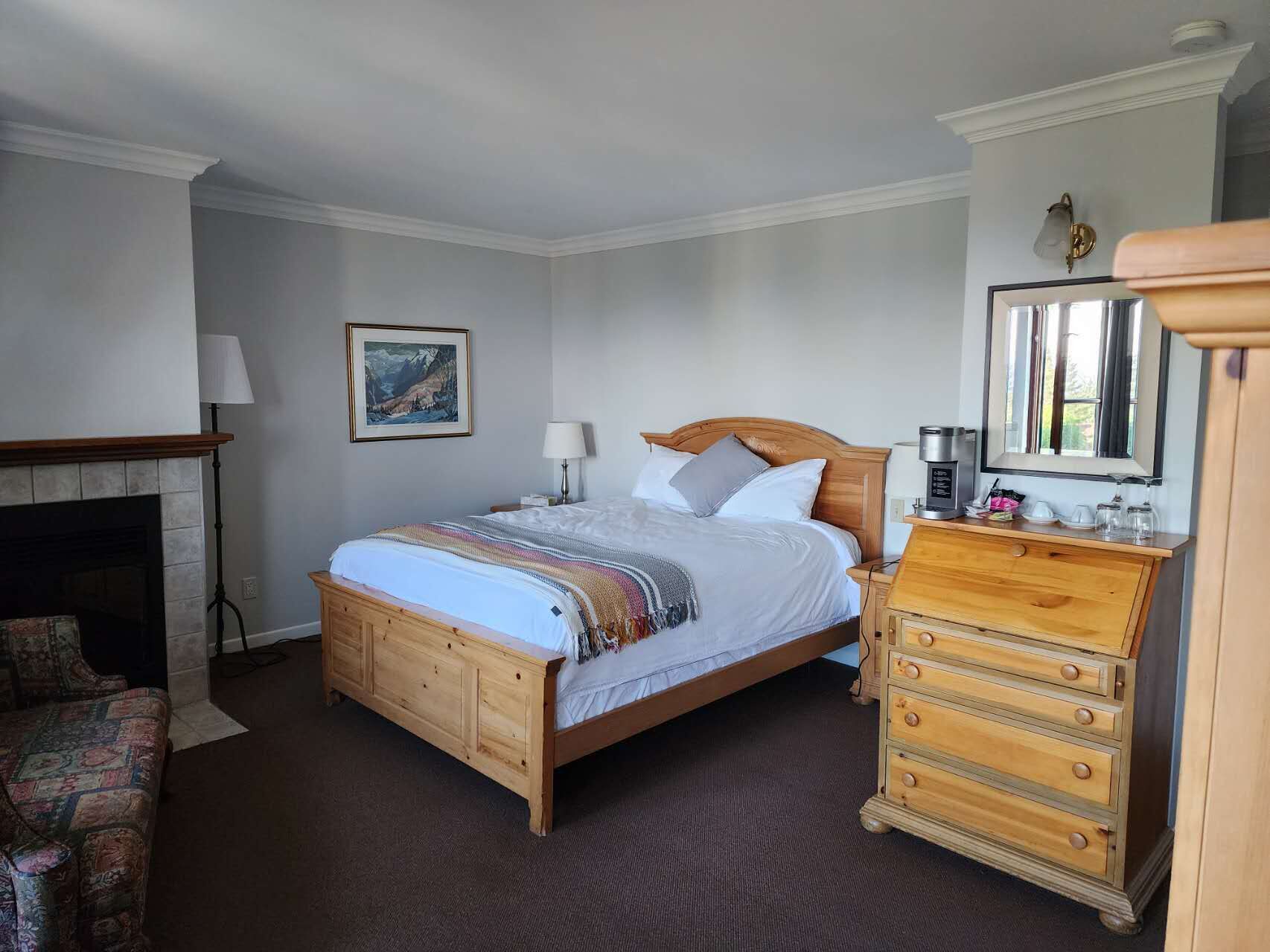 Une chambre à coucher avec un lit en bois, une commode, une table de chevet, une cheminée et un tableau encadré au mur.