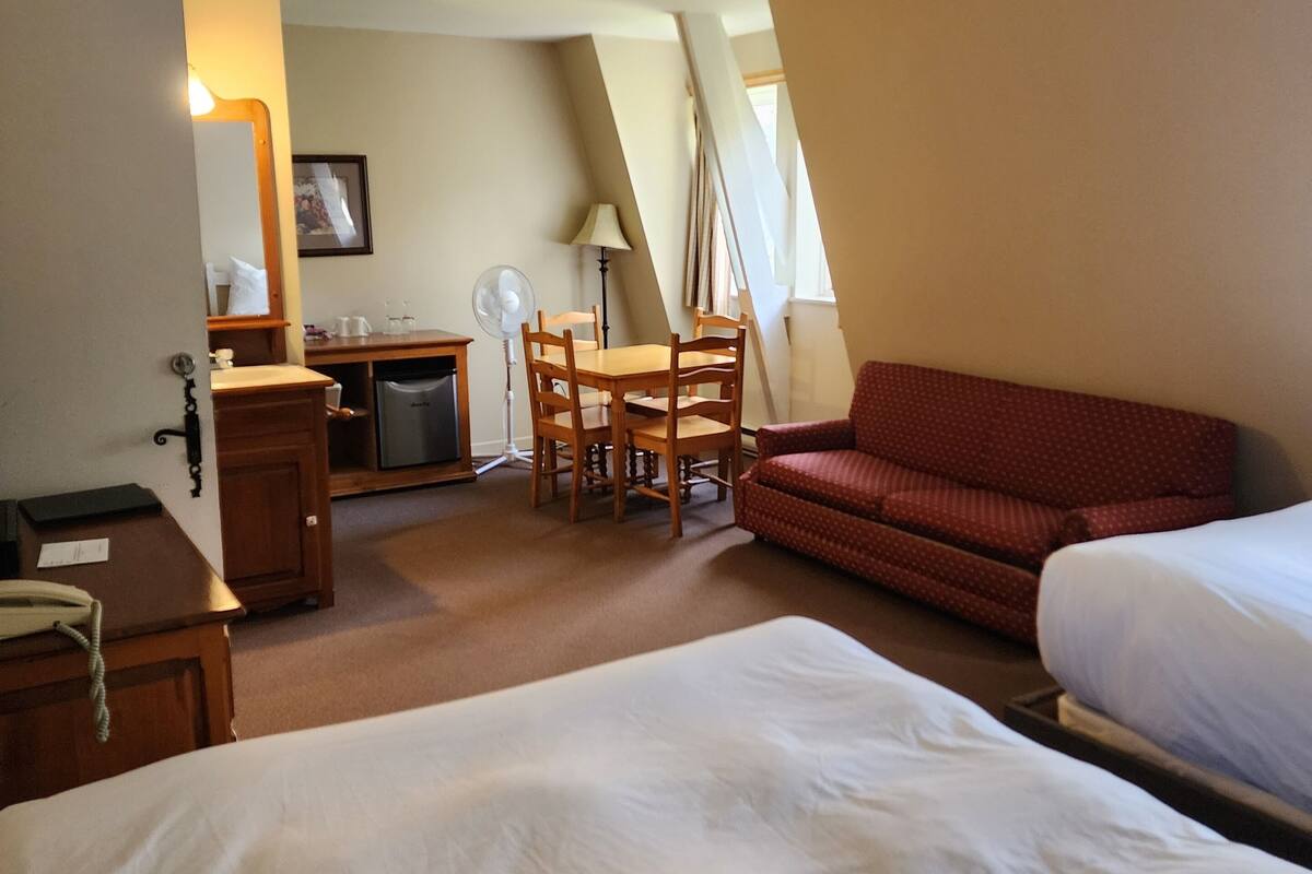 Una habitación de hotel con una cama grande, un escritorio con una silla, una kitchenette pequeña y un sofá rojo.