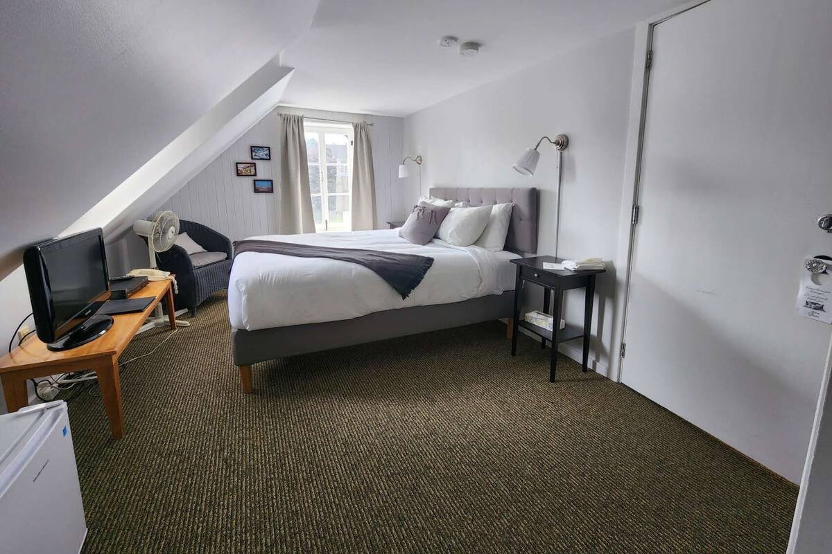 Une chambre d’hôtel avec un lit, un bureau avec un ordinateur, une chaise, une lampe et une porte.