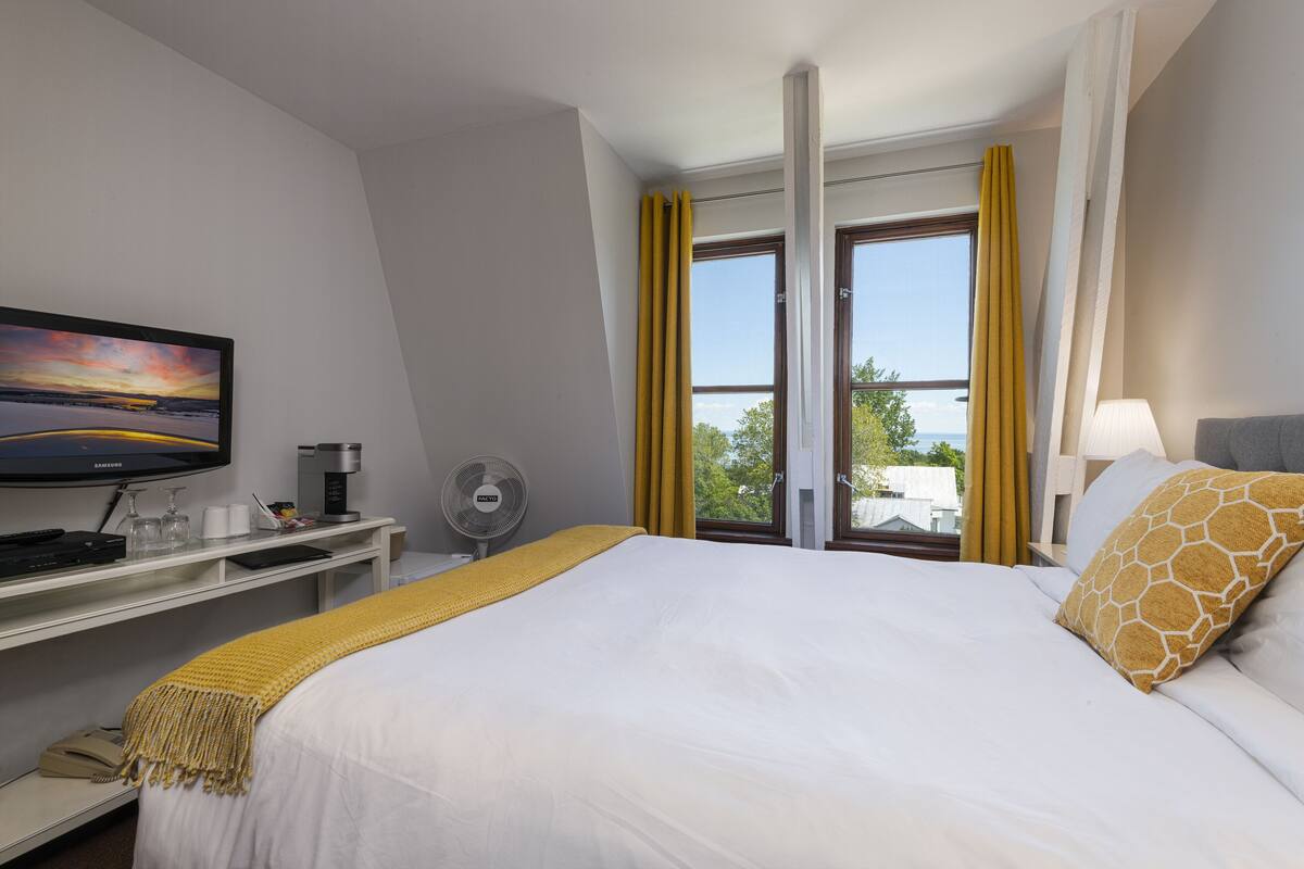 Une chambre d’hôtel avec un lit, un bureau équipé d’un ordinateur, une télévision et une fenêtre avec des rideaux.