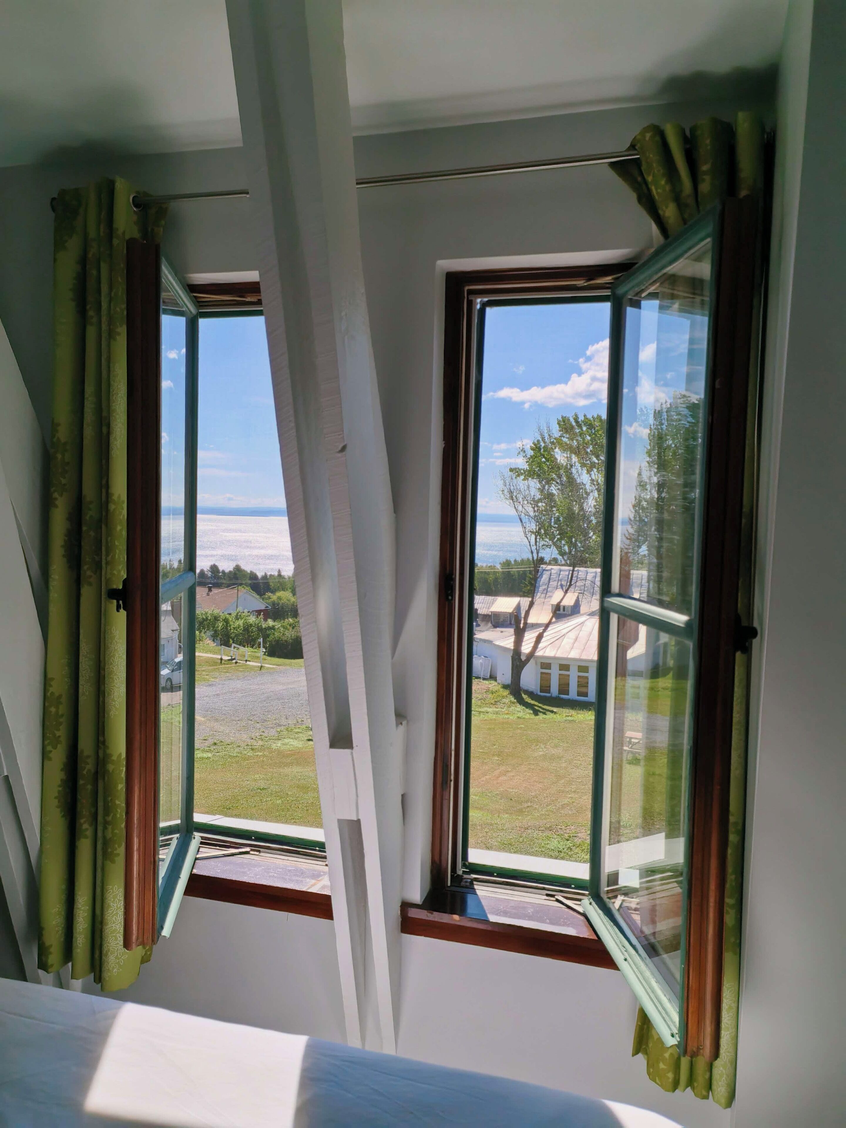 Une pièce dotée de deux fenêtres, dont l’une offre une vue sur un espace verdoyant et un bâtiment.