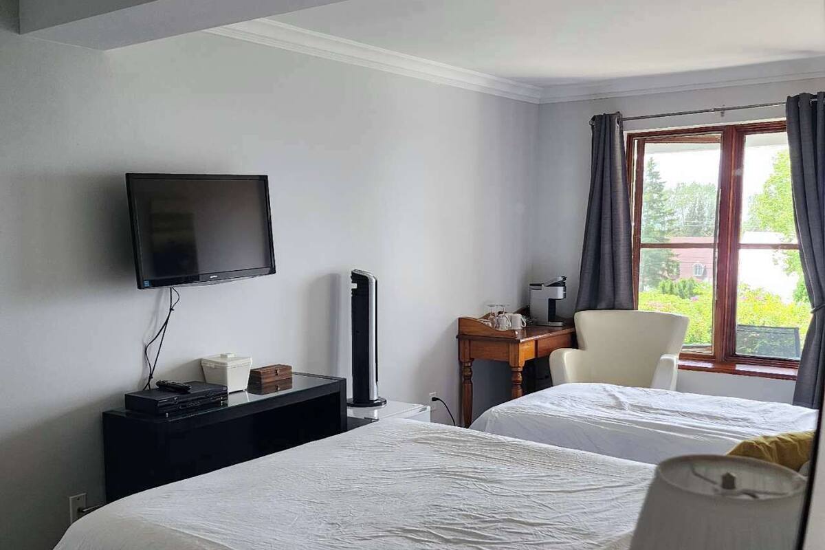 Une chambre d’hôtel avec deux lits, un bureau, une chaise, une télévision et une fenêtre avec des rideaux.