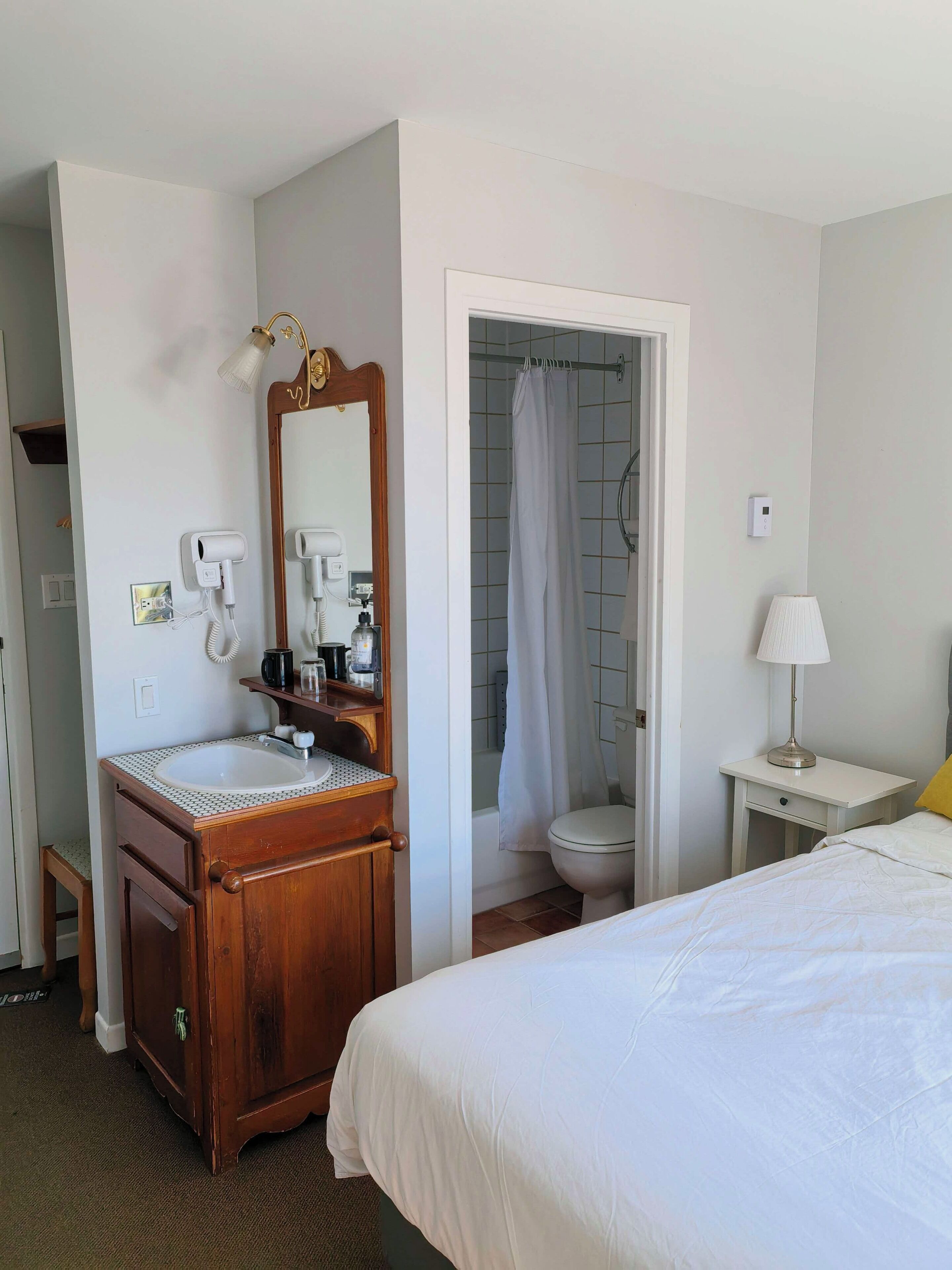 Ein Hotelzimmer mit einem Holznähtisch, einem Spiegel, einem Waschbecken, einer Toilette, einer Dusche und einem Bett.
