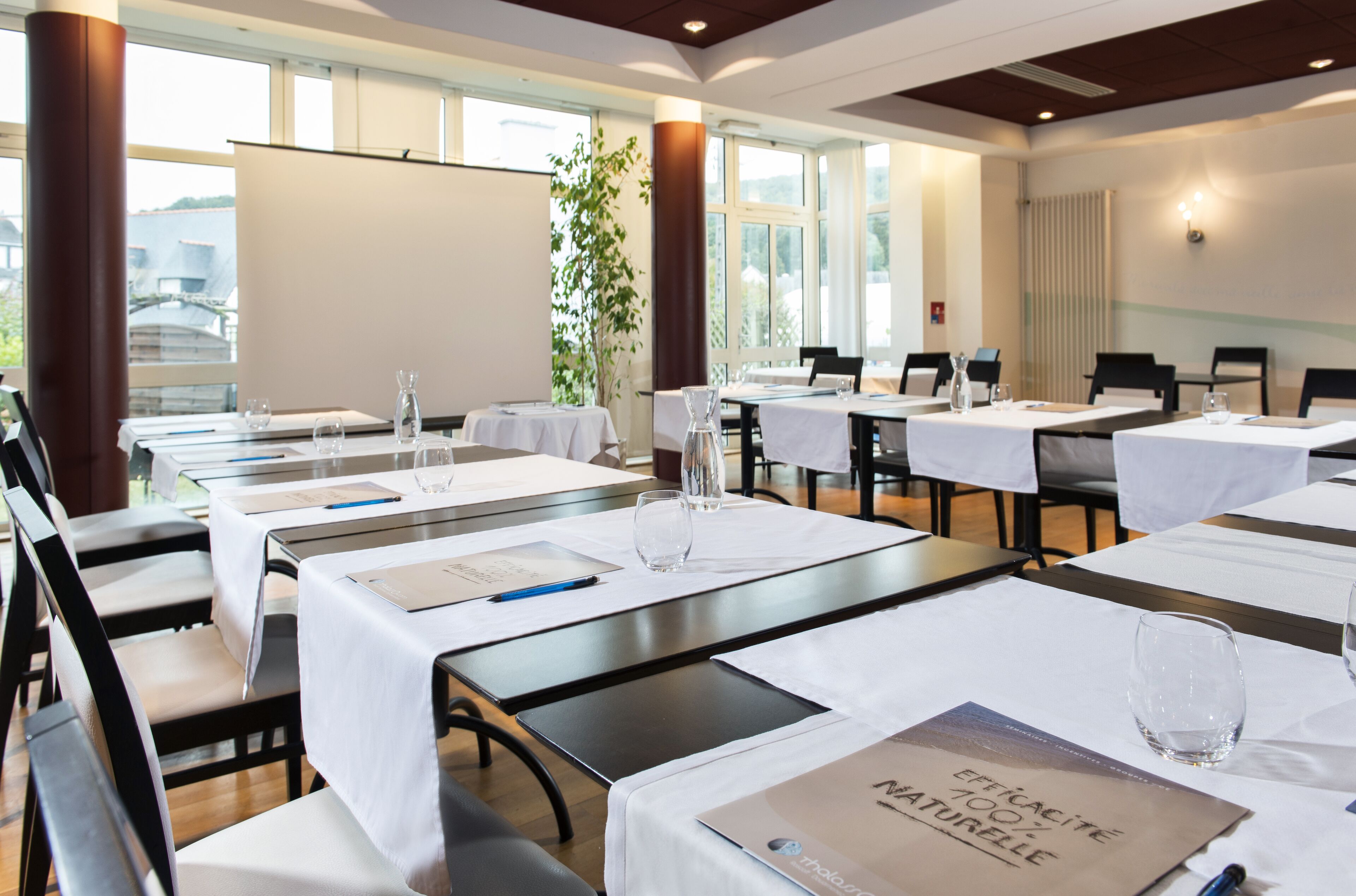 A conference room with tables set for a meeting, equipped with nameplates, water glasses, and laptops.