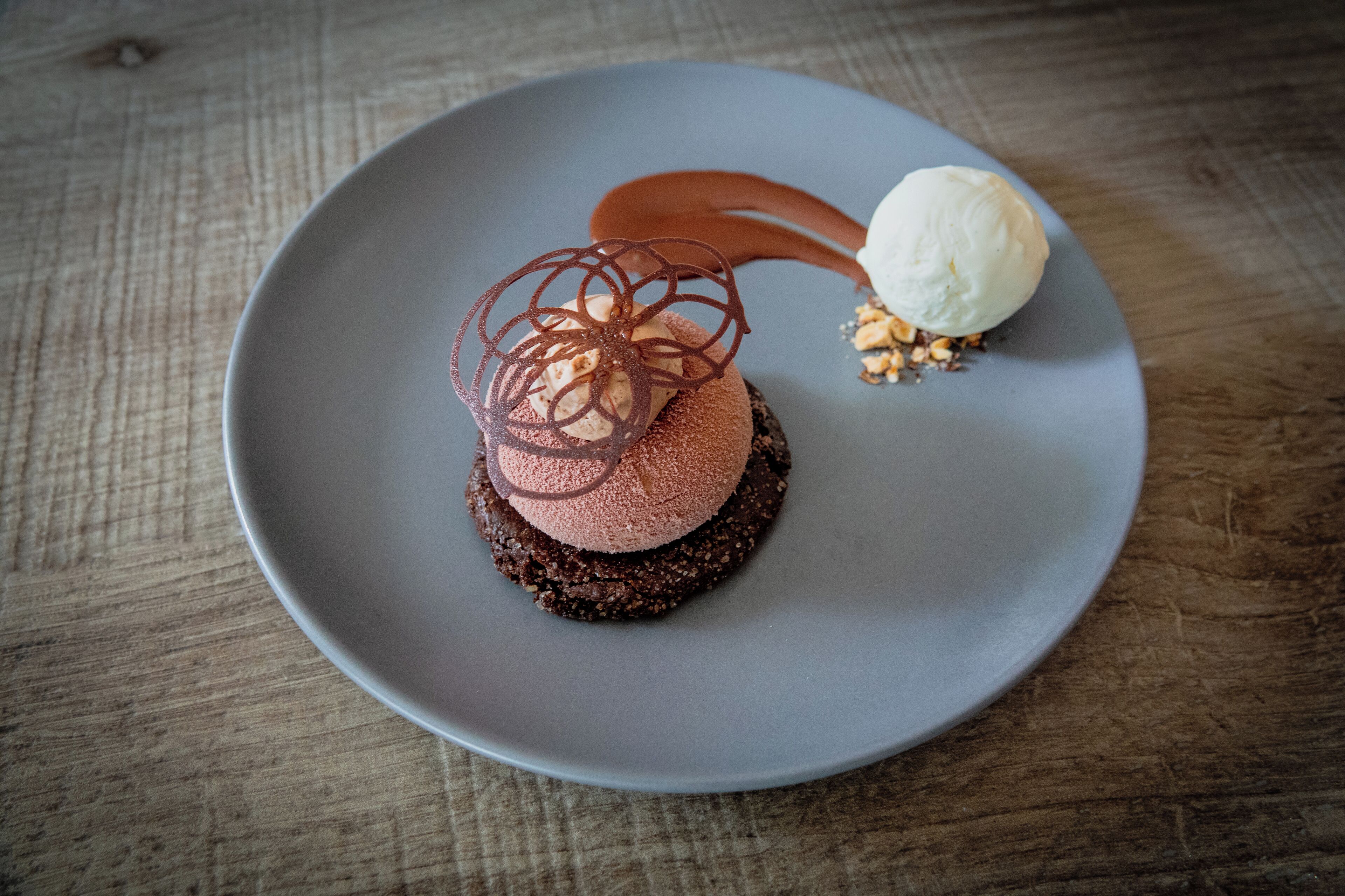 A dessert on a plate with a chocolate base, a scoop of ice cream, and a caramel drizzle.
