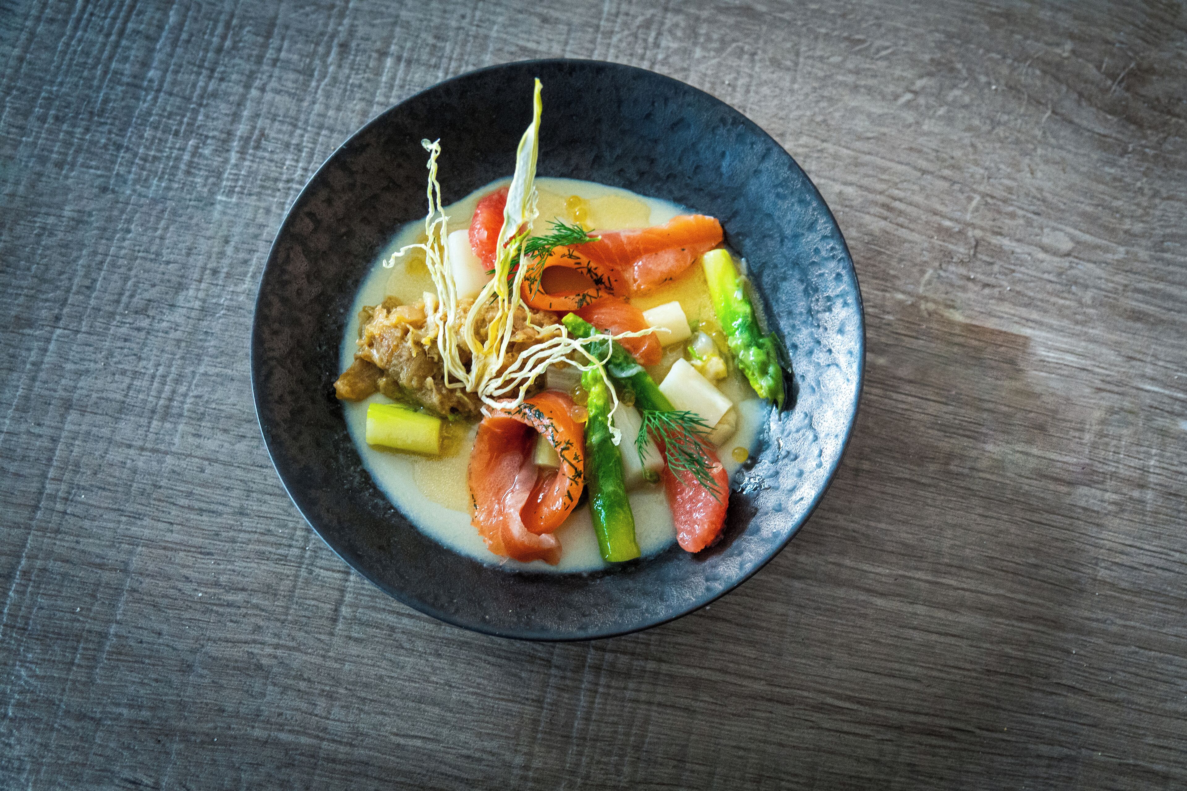 Eine Schüssel Suppe mit Gemüse und Lachs auf einem Holztisch.