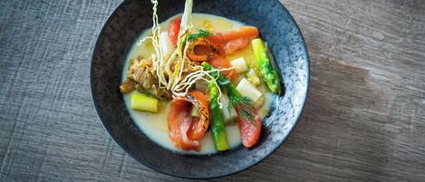 Un tazón de sopa con verduras y salmón sobre una mesa de madera.