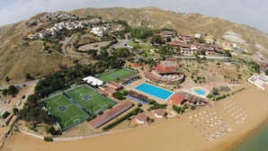 An aerial view of a coastal resort with a beach, a pool, sports facilities, and a mountainous backdrop. -  Fruit Village Crotone Casarossa (Crotone)