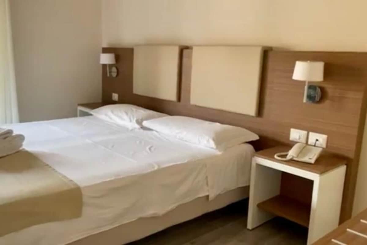 A neatly made bed with white linens, a bedside telephone, and a lamp on a nightstand.