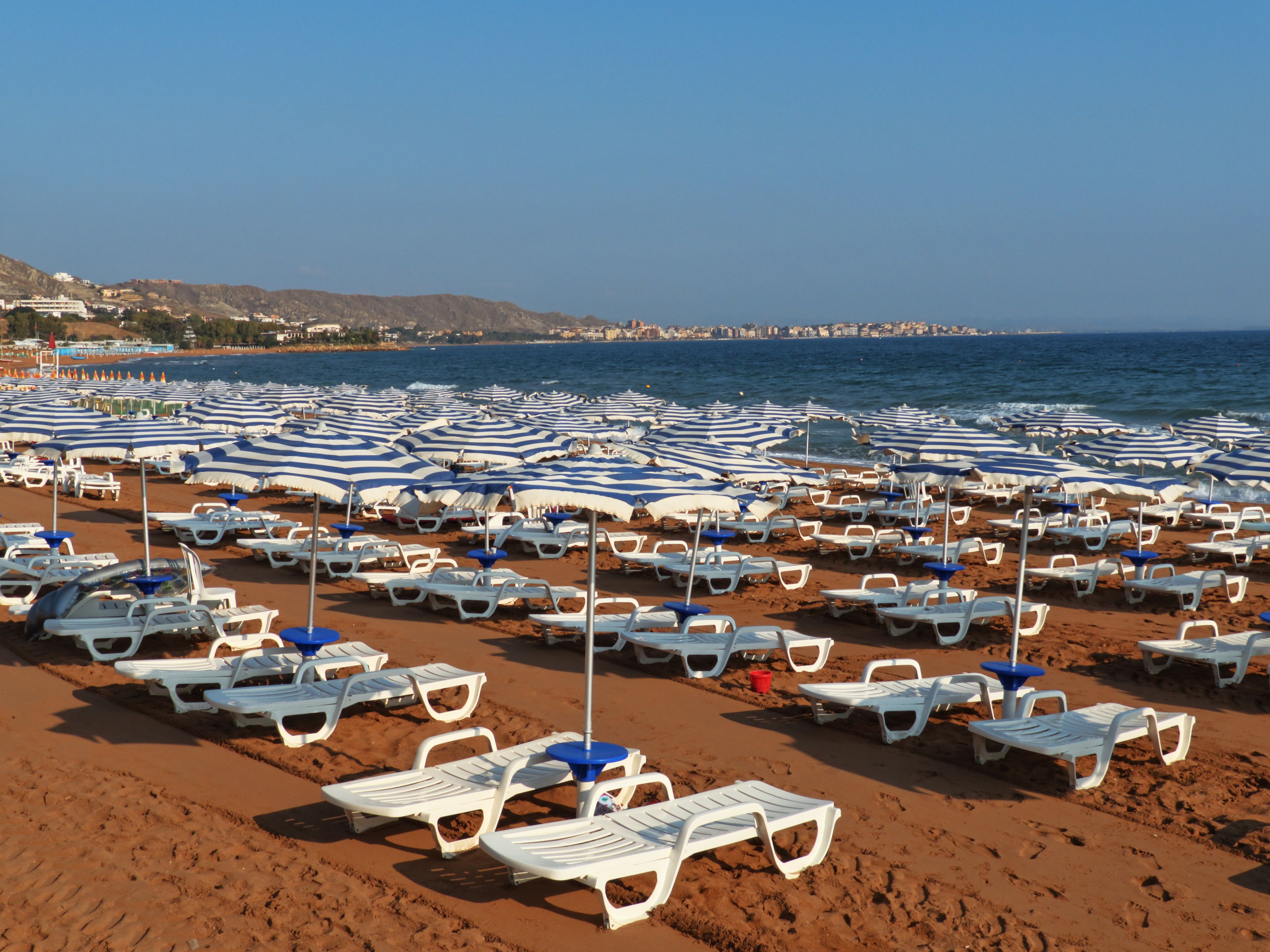 A beach with rows of white sun loungers and blue and white striped umbrellas.