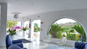 A modern hotel lobby with a glass coffee table, blue sofas, and a view of greenery outside. -  Fruit Village Crotone Casarossa (Crotone)