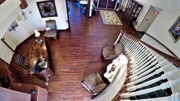 A spacious living area with a wooden floor, a staircase with white balusters, and a dining area with chairs and a table.