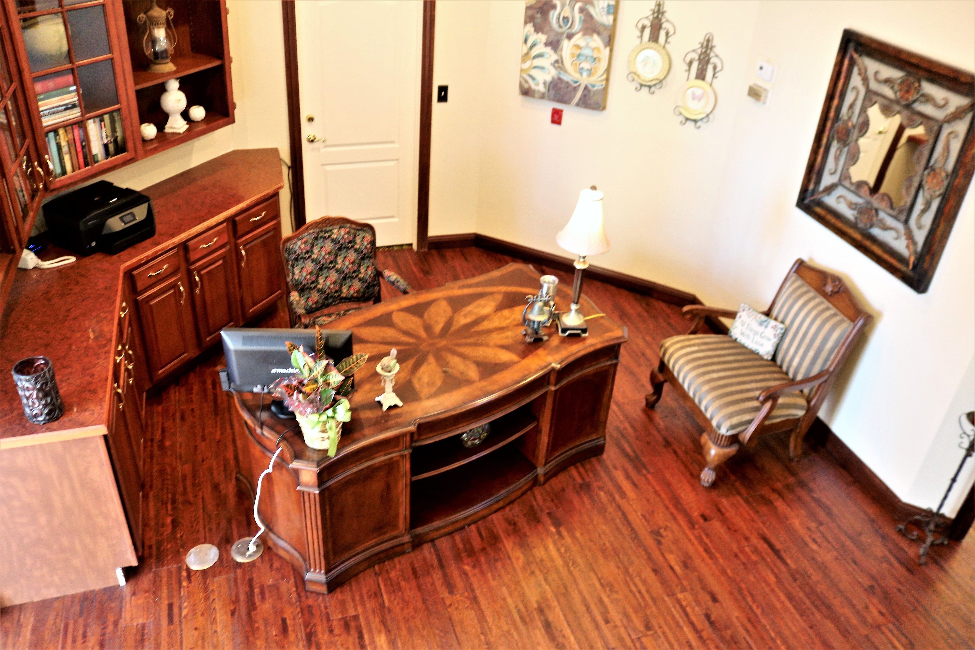 A room with a wooden desk, a chair, a lamp, and a bookshelf.