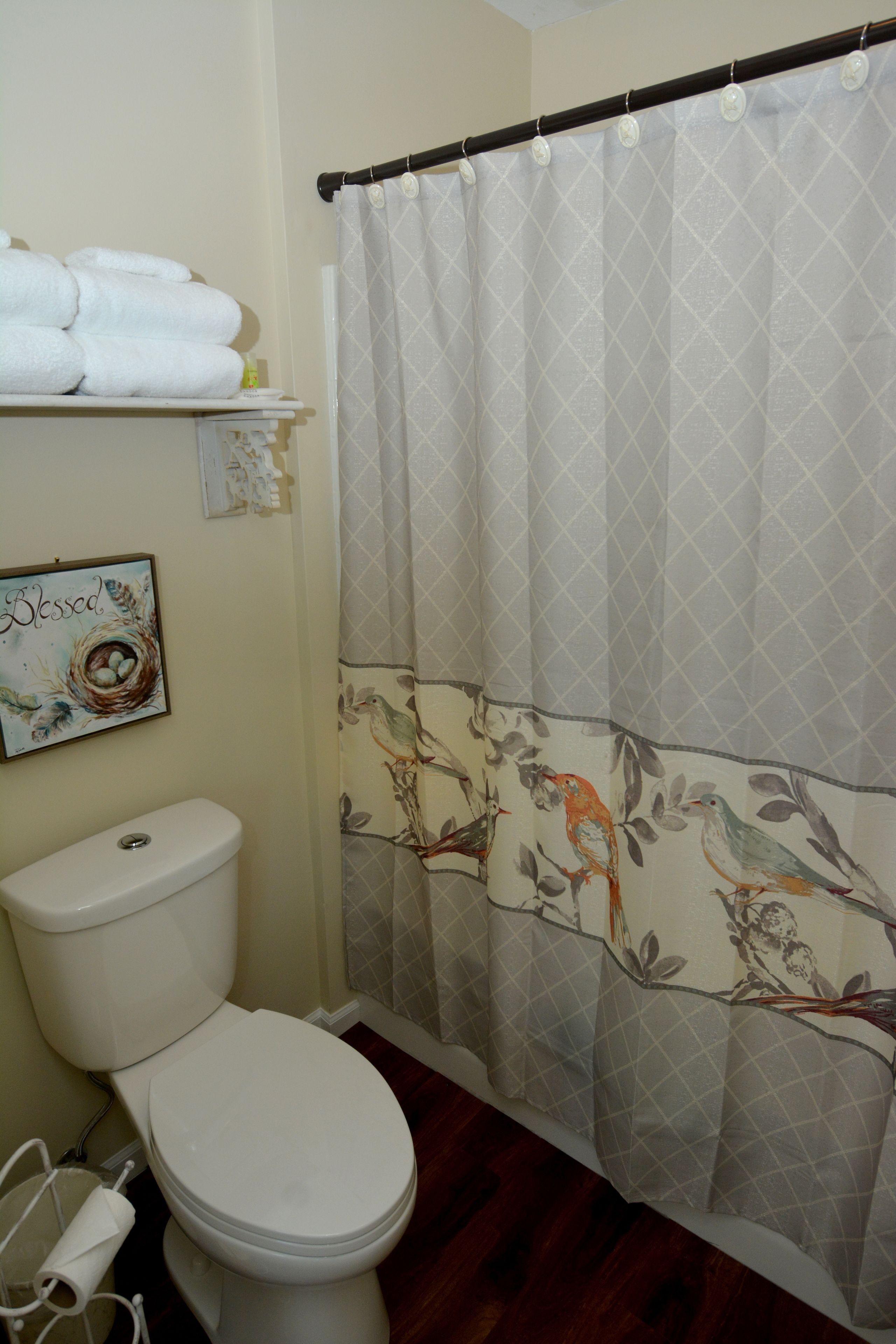 A bathroom with a toilet, a shower curtain with bird patterns, and a 'Blessed' sign on the wall.