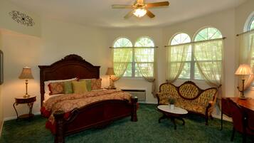 A bedroom with a large bed, a chair, a table, and a ceiling fan.