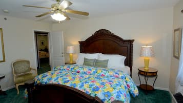 A bedroom with a wooden bed, floral bedspread, two bedside lamps, a chair, and a ceiling fan.