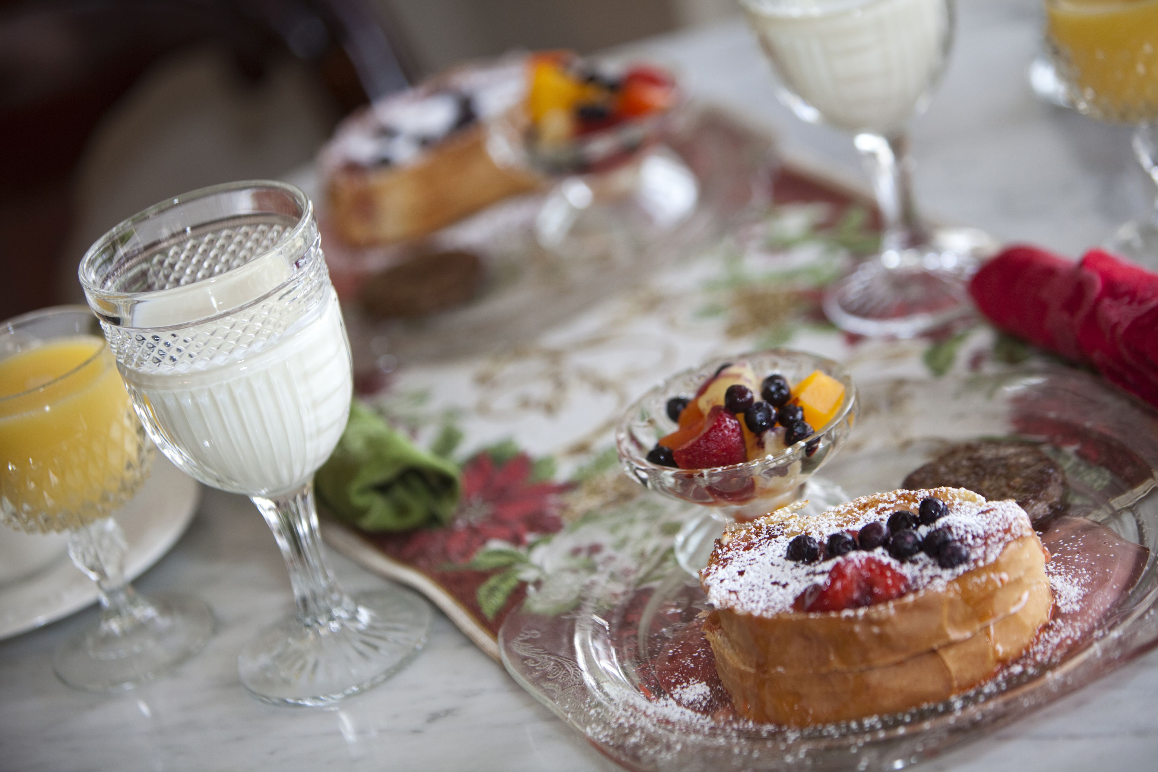 A breakfast setting with a fruit bowl, a glass of orange juice, and a pastry on a floral tablecloth.