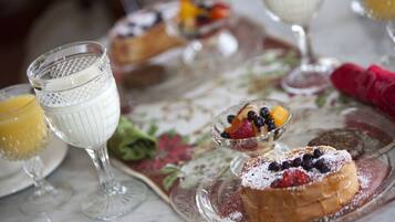 A breakfast setting with a fruit bowl, a glass of orange juice, and a pastry on a floral tablecloth.