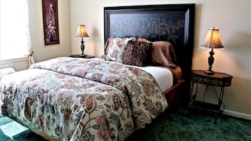 A bedroom with a large bed, two bedside tables with lamps, a framed artwork on the wall, and a patterned bedspread.