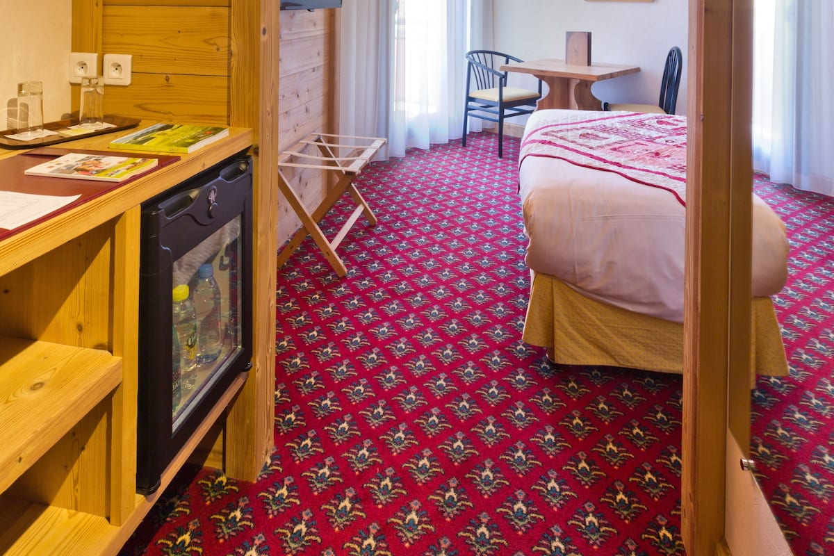 Una habitación de hotel con techo de madera, una cama sobre alfombra roja estampada, un escritorio con computadora y una silla.