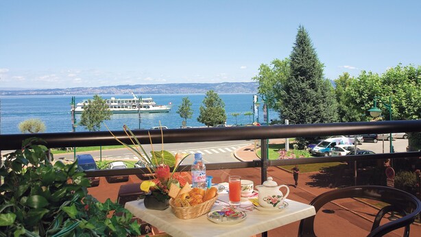Ein Balkon mit Frühstückstisch, Blick auf einen See mit einem Boot und Stadtansicht.