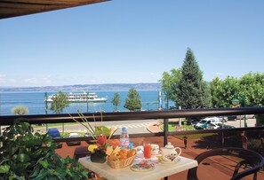 Un balcon avec une table préparée pour le petit-déjeuner, donnant sur un lac où l’on aperçoit un bateau et le paysage urbain.