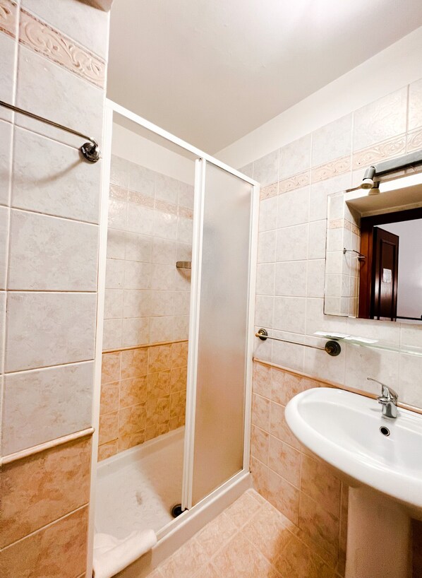 A bathroom with a glass shower enclosure, a sink, and a mirror.