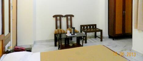 A hotel room with a bed, a small table with chairs, a wardrobe, and a wall-mounted light fixture.