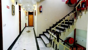 Un pasillo de hotel con suelo de mármol, una escalera con barandillas blanco y negro, y un extintor montado en la pared.