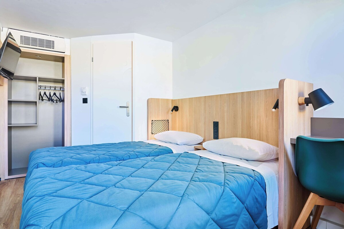 A hotel room with two beds, a wooden headboard, a desk, and a chair.