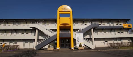 A building with a prominent yellow entrance, two staircases, and a sign reading "PREMIERE CLASSE".